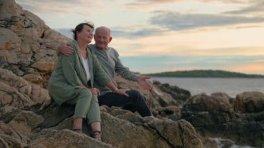 Emekliler için tatil, mutlu yaşlı kadın ve erkek turistler sıcak bir akşamda sahilde oturarak deniz kıyısının ve günbatımının tadını çıkarıyorlar.