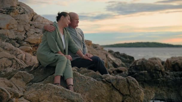 引退生活 魅力的な高齢の女性と男性の観光客は 海への旅行を楽しんで 岩の上に座っている間日没を賞賛 — ストック動画