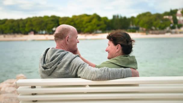 休暇中の年金受給者 海でリラックスしながら銀行のベンチに座って愛する老人と女性 — ストック動画