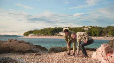 aktif yaşlı adam ve kadın sıcak güneşli bir akşamda emeklilerin tatili sırasında denize çakıl taşları atarak eğleniyorlar.