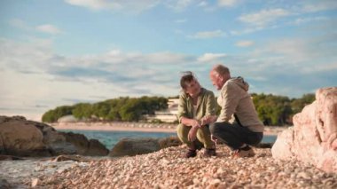 Emekliler için tatil, yaşlı çekici erkek ve kadın yaşlılar için turistik gezi sırasında kıyıda otururken denize çakıl taşları atarken eğleniyorlar.