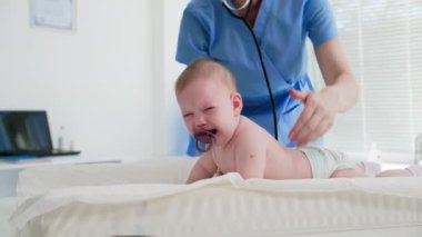 Küçük bir çocuk muayene sırasında ağlar, ilgili bir kadın doktor bebeğini kollarına alır ve pencerenin arkasını ovalar.