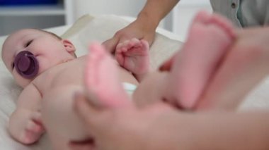 Çocukla ilgilenen kadın çocuk doktoru, bebek muayenesi sırasında elinde küçük yeni doğmuş bacaklar tutuyor.