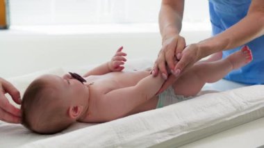 Kadın sağlık çalışanı hastane ofisinde bebek bezi takan küçük bir çocuğa masaj yapıyor.