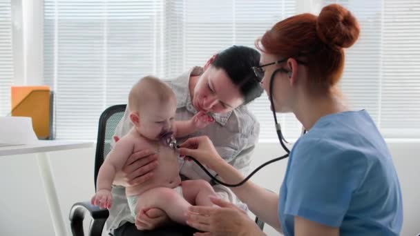 医学オフィスの小児科医との約束で小さな娘を持つ若い母親 女性医師は フォネンドスコープを使用して子供にリストアップします — ストック動画