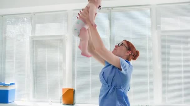喜びに満ちた医療従事者は 医師のオフィスで彼と遊んでいる間に小さな子供を投げます — ストック動画
