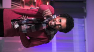 Neşeli Afrikalı Amerikalı adam gülüyor ve sıcak bir odada kameraya bakarken ekranı işaret ediyor.