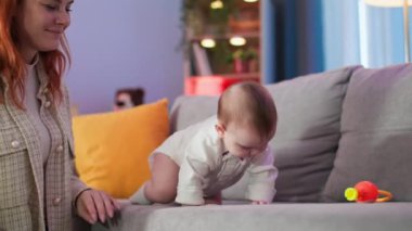 Bebeklik, çıngıraklı kanepede emeklemeyi öğrenmek, küçük kızına bakan şefkatli bir ebeveyn.