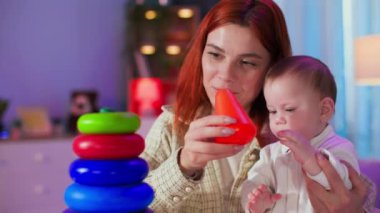 çocukluk, ilgili kadın ebeveyn ve küçük bir çocuk eğitici oyunlar oynar, renkli çemberlerden plastik piramidi bir araya getirir.