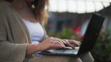 Açık havada iş, dizüstü bilgisayarda çalışan genç bir kadın açık havada bir sandalyede otururken, yakın plan.