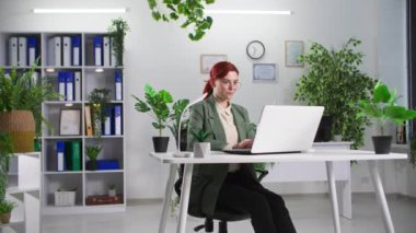Yeşil bitkilerle dolu bir ofiste dizüstü bilgisayarda çalışan genç bayan iş kadınının portresi.