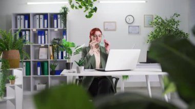 Çevre dostu ofis, genç iş kadını yeşil bitkilerle dolu bir odada bilgisayarla çalışıyor.