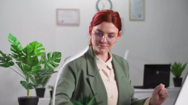 Gözlüklü genç bir kadının portresi bilgisayarda çalışıyor ve ofiste bir masada oturmuş, gülümseyip kameraya bakarken not defterine notlar alıyor.