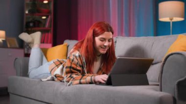 Genç bir kadın, sosyal ağlarda arkadaşlarıyla sohbet ederken tablet klavyesinde yazı yazıyor ya da rahat bir odada kanepede uzanmış yemek siparişi veriyor.