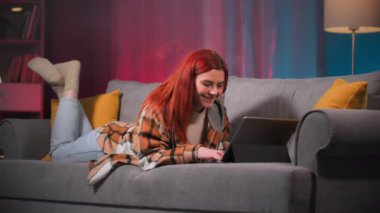 Kadın tabletle rahatlıyor, arkadaşlarıyla mesajlaşıyor akşam evde dinlenirken yatakta uzanıyor.