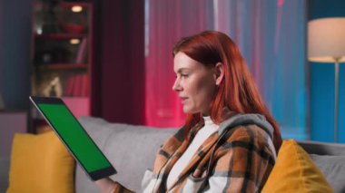 Genç bir kadın akşamları rahat bir odada otururken tablet ekranda video aracılığıyla konuşuyor, kromakey.