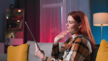 Çevrimiçi iletişim, rahat bir odada kanepede otururken video konferansında konuşan genç bir kadın.