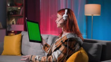 Modern iletişim türü, mikrofonu ve kulaklığı olan genç bir kadın rahat bir odada, Chroma Key 'de, tablet üzerinden video ile konuşuyor.