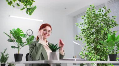 Çevre dostu bir ofiste bilgisayarın başında çalışan, gülümseyen ve kameraya bakan genç bayan çalışanın portresi.