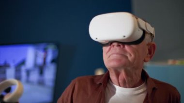 Modern yaşlı adam rahat odasında sanal gerçeklik gözlükleriyle aktif sanal oyunlar oynuyor.
