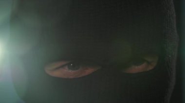 Soygun ve soygun, kar maskeli şüpheli bir adam elinde fenerle karanlık odaya bakıyor, yakın plan.