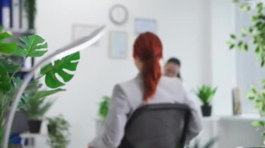 Gözlüklü gülümseyen kadın sandalyeye biner ve mutlu bir ruh hali içinde ofiste çalışmaya başlar.