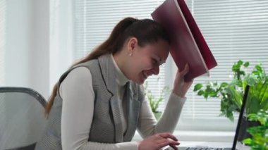 İşte eğlenceli zamanlar, gülümseyen genç bir kadın dizüstü bilgisayarda çalışırken kendini dosyayla kapatıyor çünkü meslektaşı evrakları ofise atıyor.