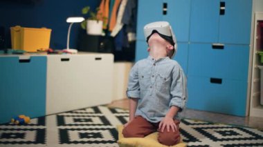 Eğlence için modern teknoloji, gözlüklü sevimli erkek çocuk rahat bir odada oturup sanal oyunlar oynayarak eğleniyor.