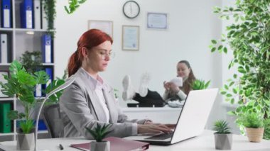 İş ortamı, dizüstü bilgisayarda çalışan bayan çalışanlar arka planda evrakları atan ofis masasında oturan.