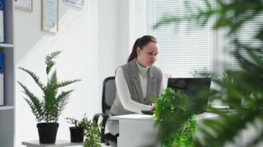 Ofisteki bilgisayarda yeşil bitkilerle çalışan bir kadın.