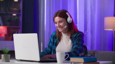 eğlence çağları, kulaklıklı genç güzel bir kadın evde bilgisayarında video oyunları oynayarak eğleniyor.