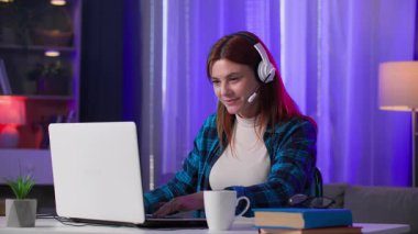 Kulaklıklı, mikrofonlu, dizüstü bilgisayarlı video oyunları oynayan, neon ışıklı odada oturan, milenyum kadınları.