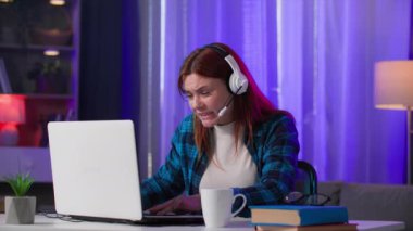 Oyun bağımlılığı, modern çağdan kalma kulaklıklı bir kadın evde akşam dinlenmesi sırasında dizüstü bilgisayarında video oyunları oynuyor.