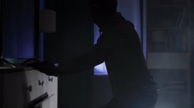 Hırsız, siyah elbiseli yetişkin bir erkek ve kar maskesi, gece değerli şeyler aramak için diğer insanların eşyalarını karıştırıyor.