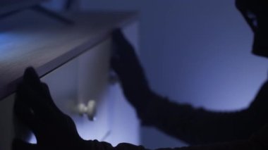 Kar maskeli ve siyah elbiseli bir soyguncu başka birinin dairesine girdi ve çekmecelerdeki çekmeceleri açtı. Gece vakti para ya da değerli eşya aramak için, yakın plan.