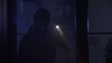 Hırsızlık, kar maskeli bir adam değerli eşyalar aramak için gece bir odaya fenerle girer.