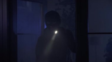 Suç ve suç, siyah elbiseli yetişkin bir adam ve elinde fener olan bir kar maskesi odaya girer ve gece etrafa bakar.