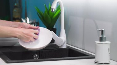 Ev işi, sünger ve köpük kullanan bir kadın mutfak lavabosunda bulaşık yıkıyor, kapat.