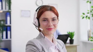 Ofiste gözlüklü, gülümseyen ve kameraya bakan çağrı merkezi çalışanının portresi.