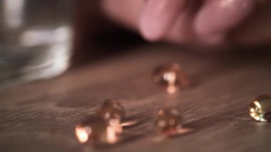 Tırnakları bakımlı, güzel kadın parmaklarının yakın plan fotoğrafı. Masada bir hap seçip, içeri alıyor. Hafif arka plan ışığı olan yarı karanlık bir odadaki haplara odaklanarak.
