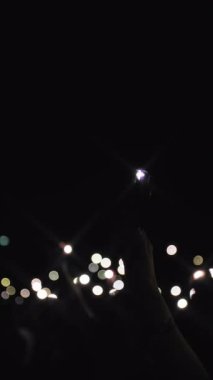 Konser ışığı gösterisi. Pek çok eğlenceli insan ellerinizi kaldırıp, telefonlarınızı el fenerleriyle tutarken, onlar da rock grubunun en sevdikleri performanslarını sergilerler. Ön planda, bir kadının eli kaldırılır, telefonu tutar ve...