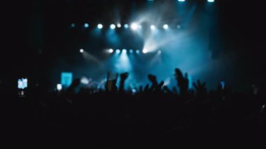 Müzikle dalgalanan hayranların karanlık silueti. Taraftarların en sevdiği rock grubunun sahne aldığı Cyan ve White Backlight Show