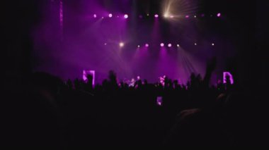 Renk dinamik ışık gösterisi. Sahne ışıklarının karşısında el sallayan hayranların karanlık silueti. Beyaz, eflatun arka plan gösterisi, hayranların en sevdiği rock grubu sahnede