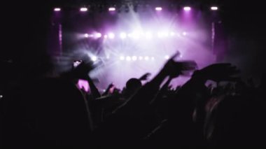 Koyu renkli siluet, el sallayan hayranların elleri, sonra da alkışlıyorlar. Magenta sahne arkası gösterisi, hayranların en sevdiği rock grubu sahnede