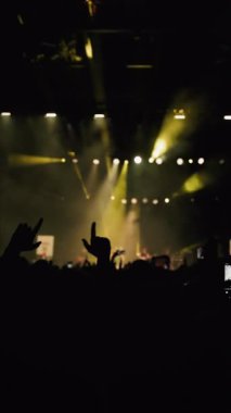 Ön plandaki kadın, el sallayarak ve dans ederek sahnenin sarı ışıklarına karşı.