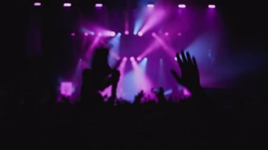 Müzik rengi ışık gösterisi. Orta boy yakın çekim. Sahne ışıklarının karşısında el sallayan hayranların karanlık silueti. Beyaz, morumsu ve mavi arka plan şovu, taraftarların en sevdiği rock grubu.