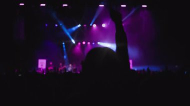 Konser müzik şovu. El sallayan hayranların karanlık silueti. Önplanda genç kadınlar yükselen eller ve güçlü duygularla dans ediyorlar. Magenta ve mavi arka plan şovu, taraftarların favorisi.
