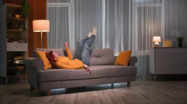 Akşamları, rahat giyimli mutlu kızıl saçlı kadın kanepede zıplıyor. Oturma odasındaki sarı yastığa uzanıp dinleniyor. Ilık ve loş ışıklandırmalı.. 