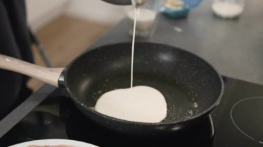 Bir ev mutfağında, bir aşçı fırının üzerindeki ısıtılmış bir tavaya hamur döker. Sonra tavayı yana doğru eğerek hamurun eşit şekilde yayılmasına yardım eder. Tavayı fırına koyduktan sonra....