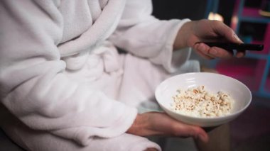 Akşamları, kanepede oturan beyaz sabahlıklı bir adam uzaktan kumandayı bir kenara koyar ve televizyon izlerken patlamış mısır yer.